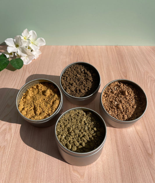 4 Metal tins containing different herb blends sitting wood table next to flowers