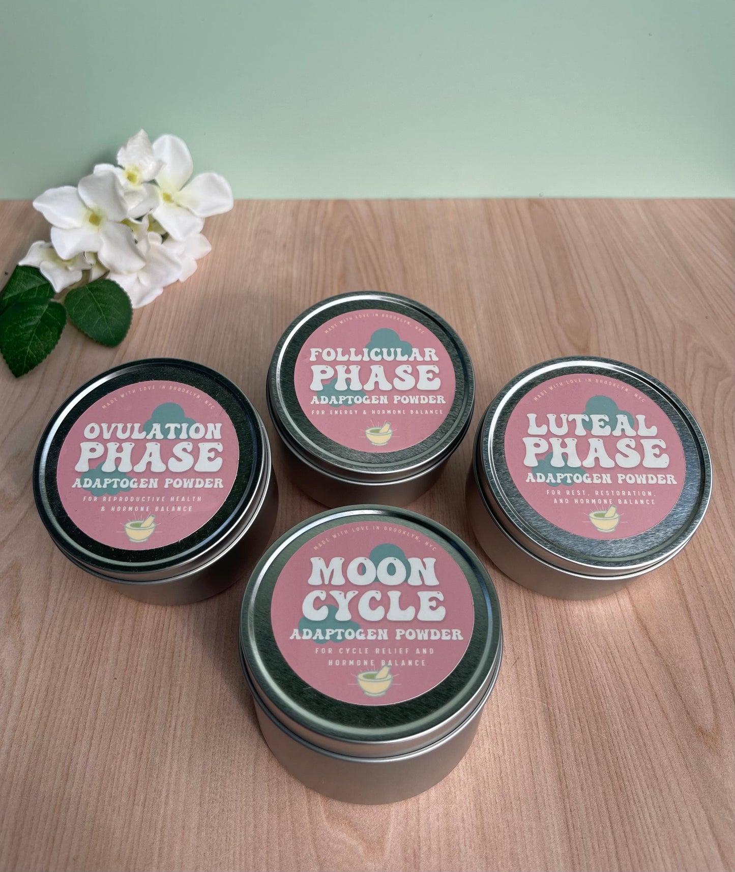 4 metal tins sitting on wood table next to flowers. One tin reads Ovulation phase, one tin reads Follicular phase, one tin reads luteal phase, one tin reads moon cycle