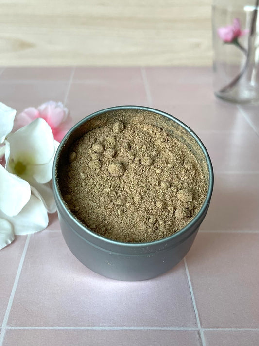 Metal tin containing herbal powder blend sitting on tile counter next to flowers
