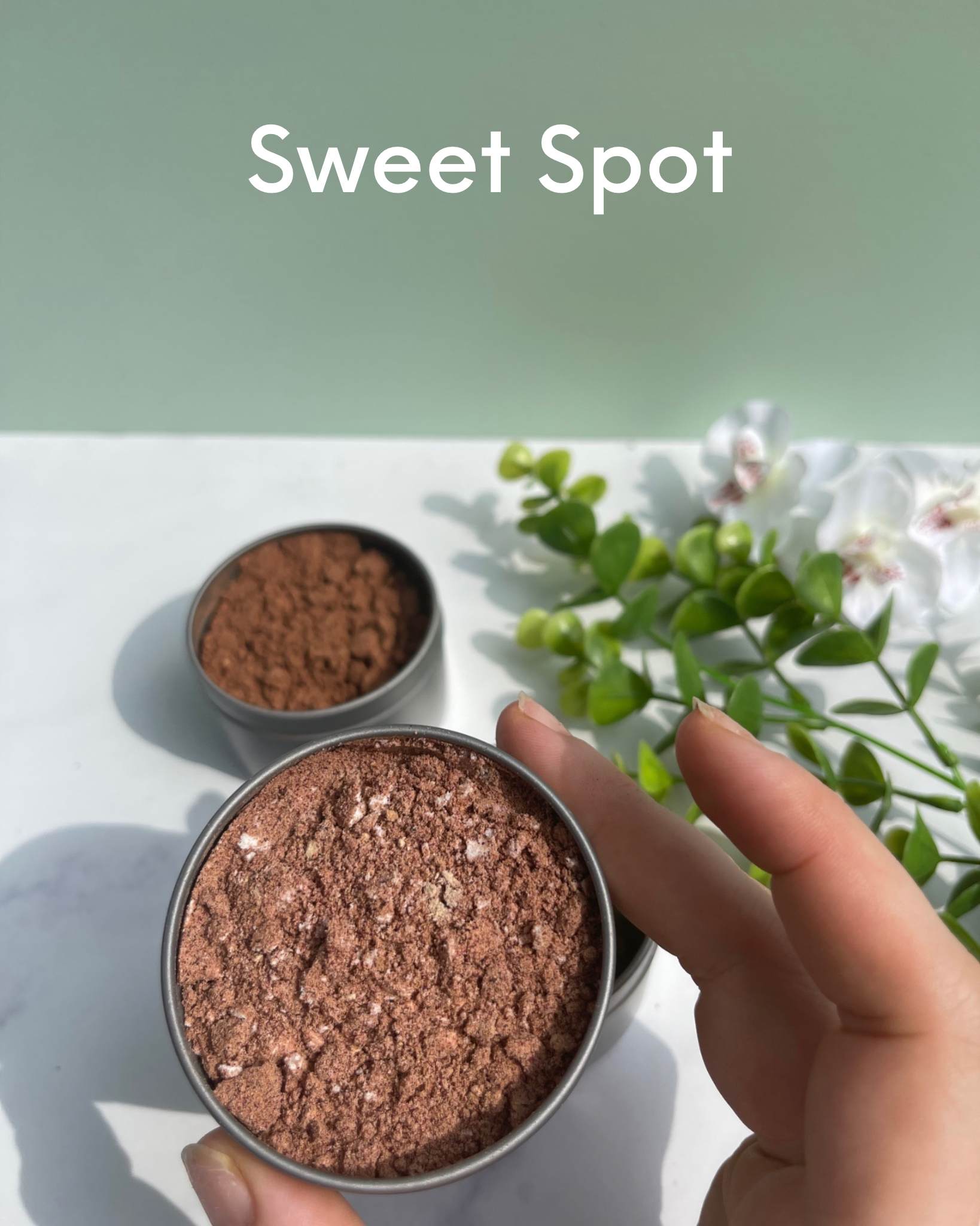 Reads: Sweet Spot. Foreground : hand holding metal tin containing herbal blend. Background: 2 metal tins containing herb blends sitting on marble counter next to flowers
