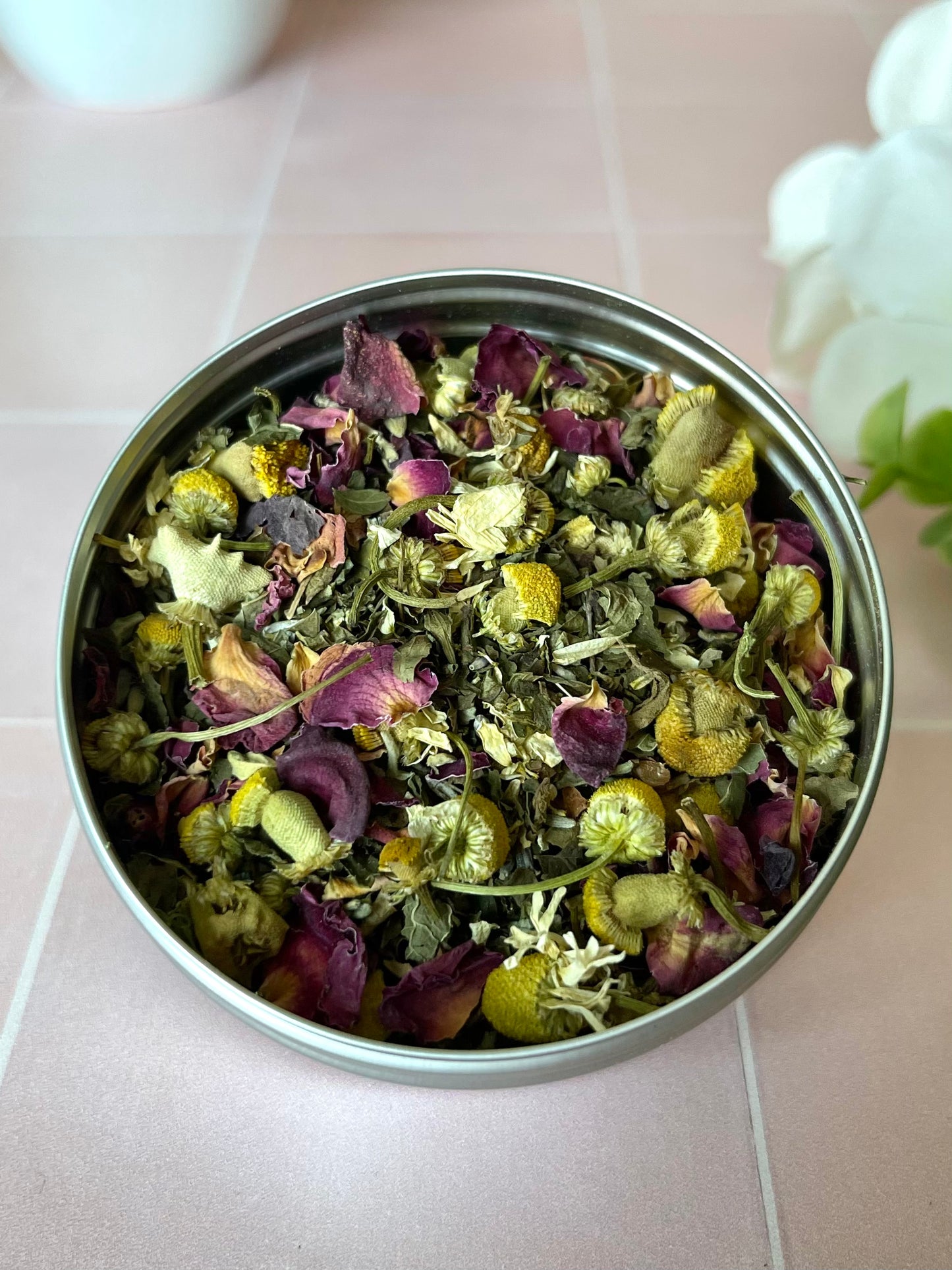herbs in metal tin on wood counter next to flowers